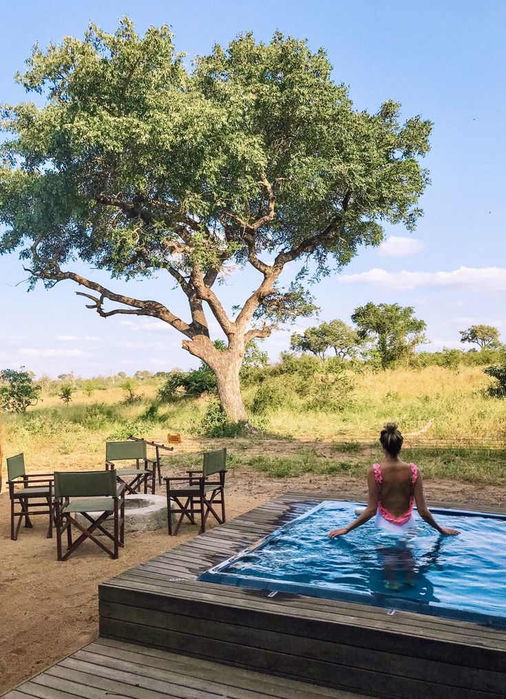 a woman in a pink bathing suit sitting on a wooden platform next to a tree