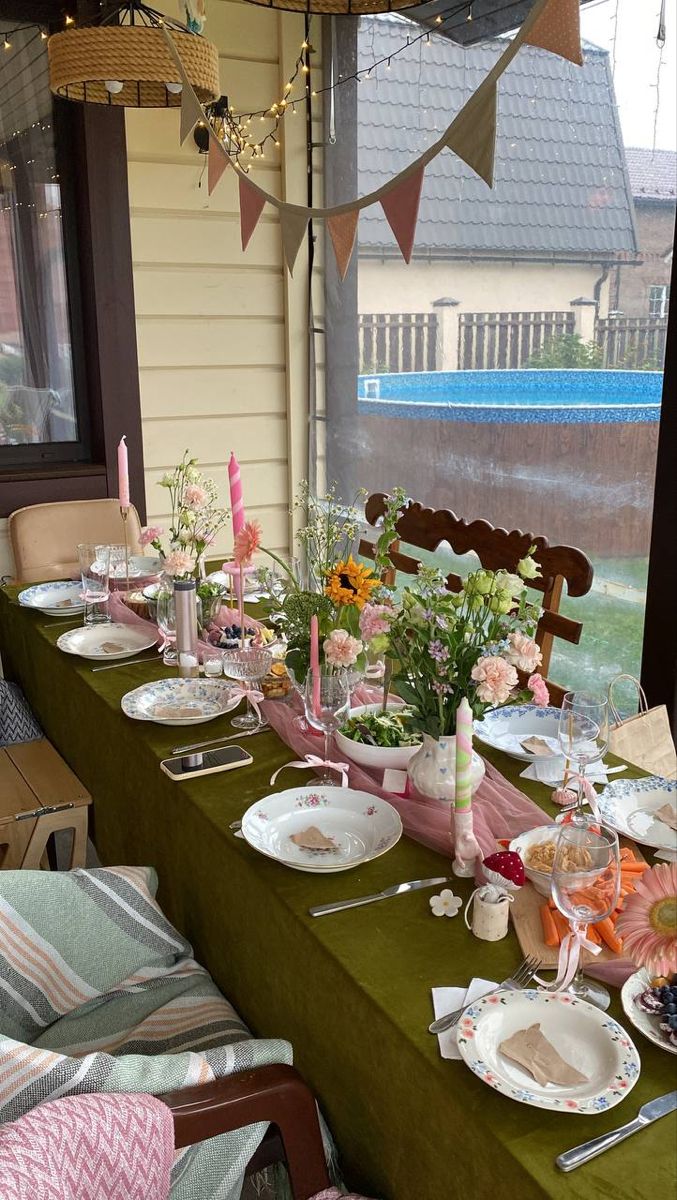 a long table with plates and flowers on it in front of a patio area that is decorated with bunting