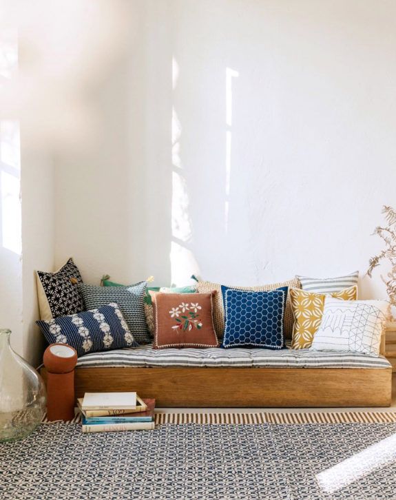 a couch with many pillows on it in front of a white wall and window sill