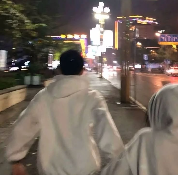 two people are walking down the street at night with raincoats on and one is wearing a white jacket