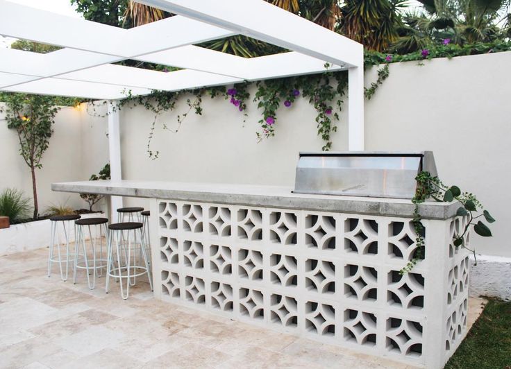 an outdoor bar with stools and plants on the back wall, in front of a white fence