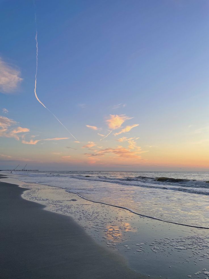 an airplane flying over the ocean at sunset with waves coming in and people walking on the beach