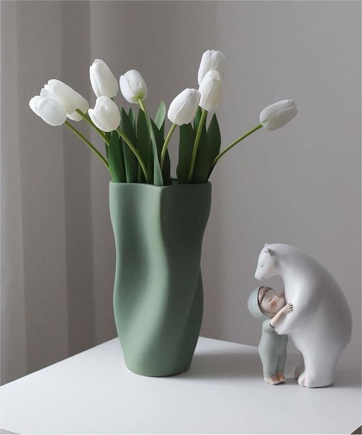 there is a vase with white flowers in it and a small bear figurine next to it