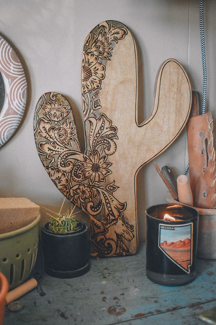 a wooden cactus sitting on top of a table next to potted plants and candles