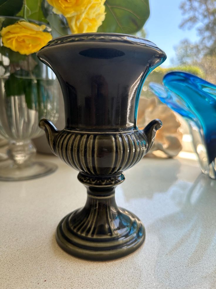 a blue glass vase sitting on top of a table next to yellow and white flowers