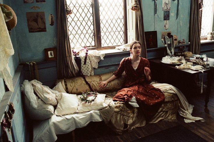 a woman sitting on top of a bed in a room with lots of clutter