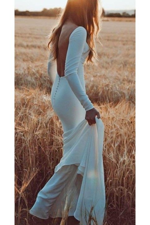 a woman in a white dress is standing in a field with her back to the camera