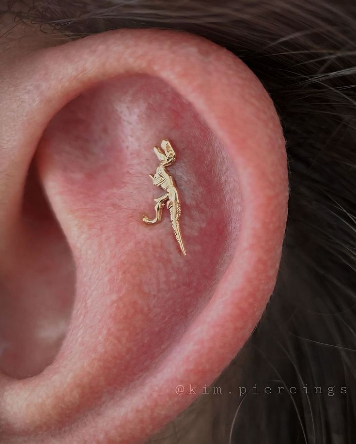 a small gold lizard earring on top of a person's ear, with the word