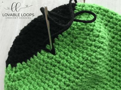 a green and black crochet bag with a pair of scissors on it's side