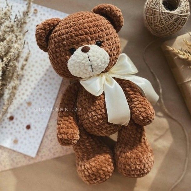 a brown teddy bear sitting on top of a table next to some twine spools