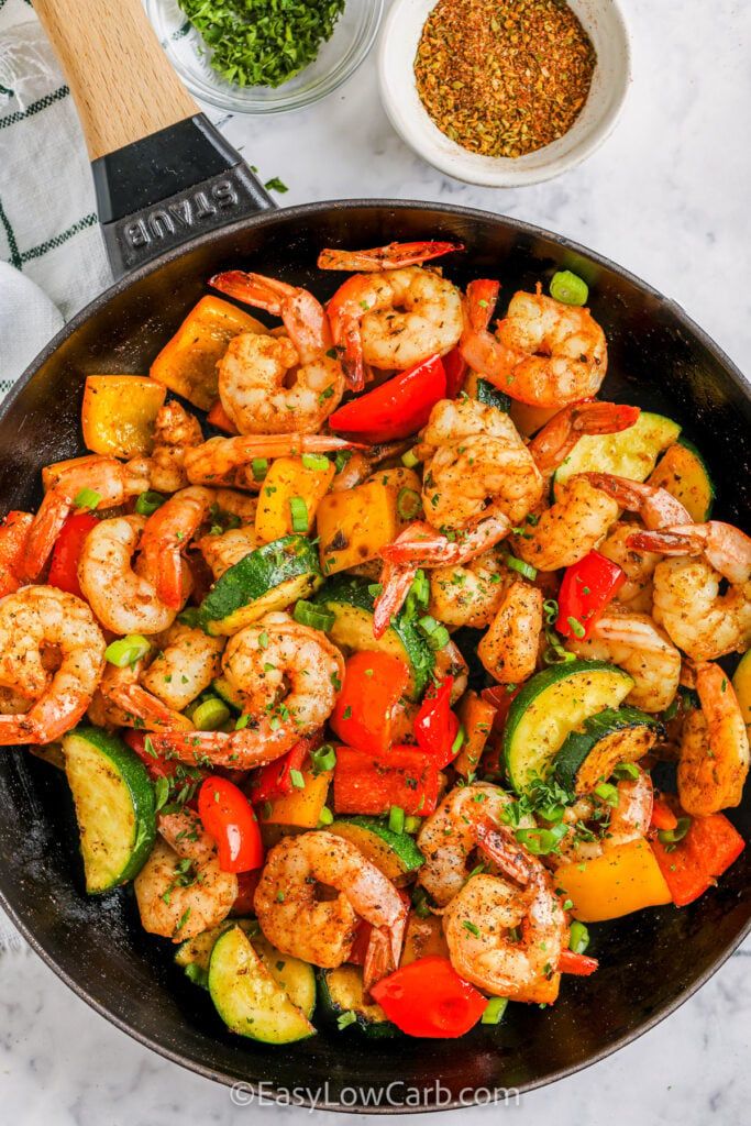 shrimp, zucchini and peppers in a skillet with seasoning on the side