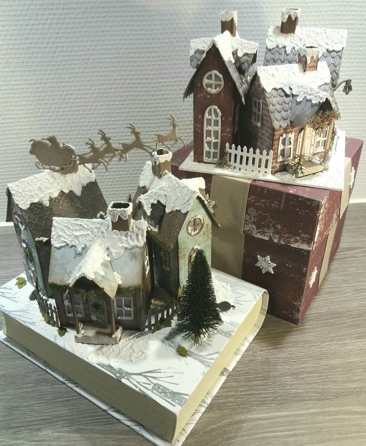 a book with some houses on top of it next to a christmas tree and sleigh