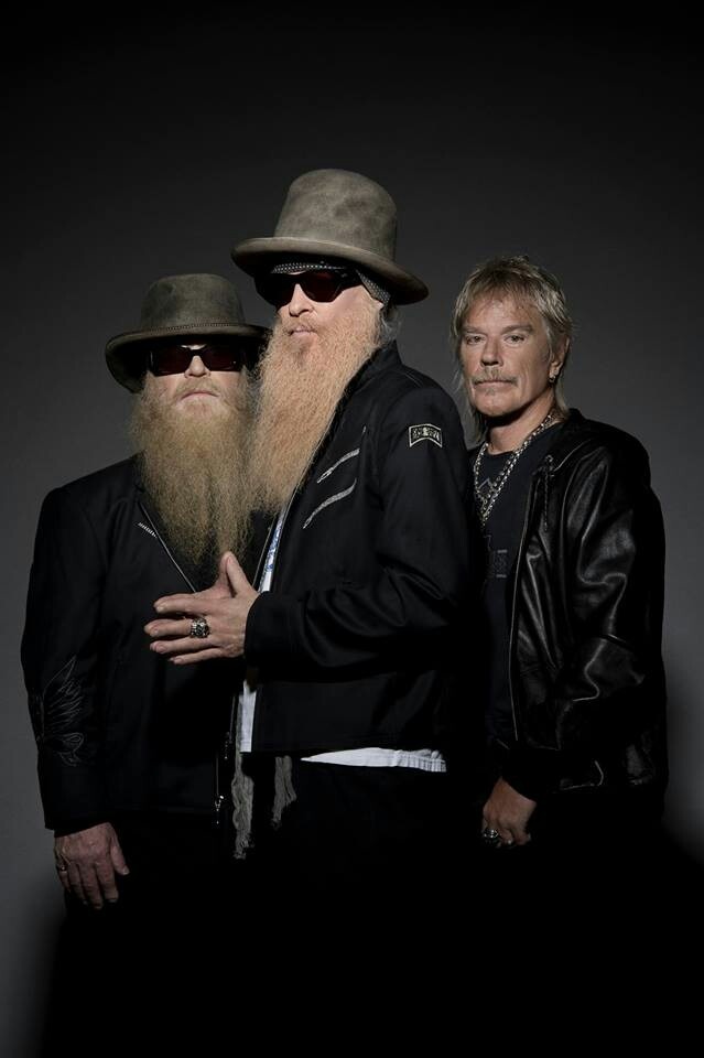 two men with long beards standing next to each other in front of a dark background