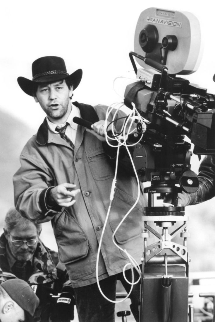 black and white photograph of man with camera on tripod in front of movie set