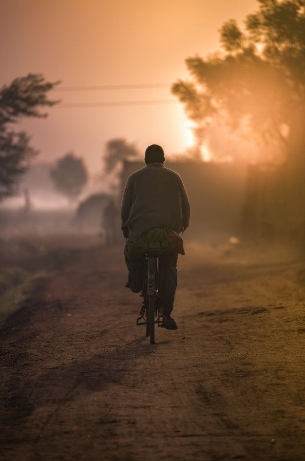 a man riding a bike down a dirt road at sunset or dawn with the sun behind him