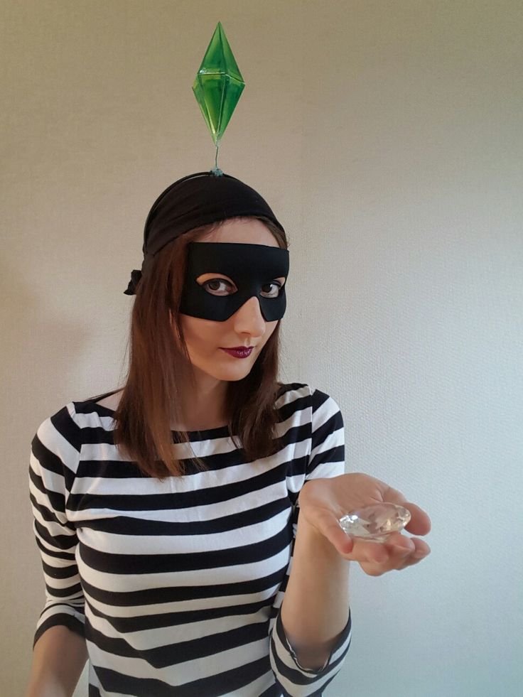 a woman wearing a black mask and holding a wine glass in her right hand with a green pyramid on top of her head