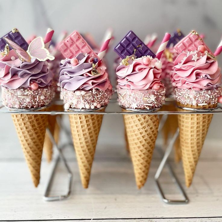 four cones with pink and purple frosting in them on a metal stand, each topped with chocolate wafers