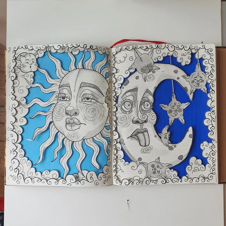 an open book with drawings on the pages and in front of it is a drawing of two sun and moon faces