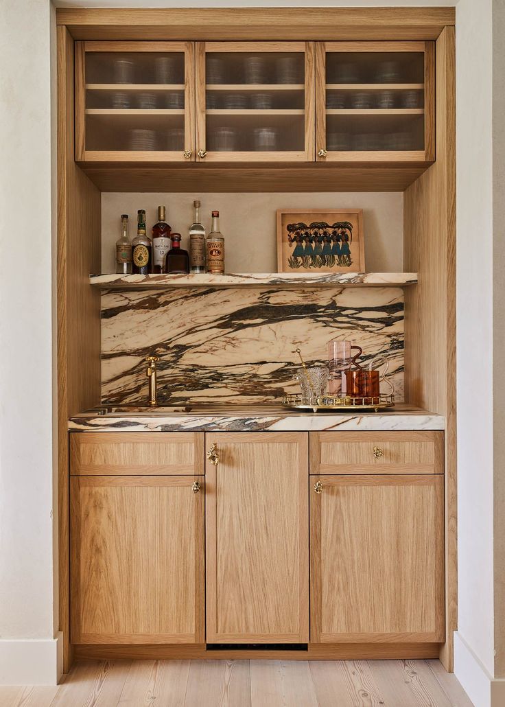 a kitchen with wooden cabinets and marble counter tops on the wall, along with liquor bottles