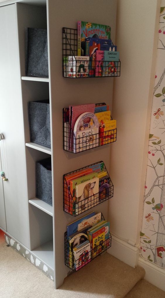 a book shelf filled with books next to a white wall and carpeted floor in a child's room