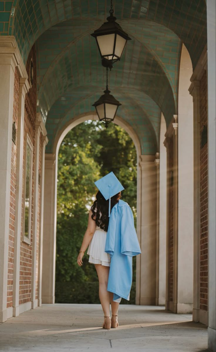 a woman in a graduation gown and cap walks under an archway with a light blue robe on