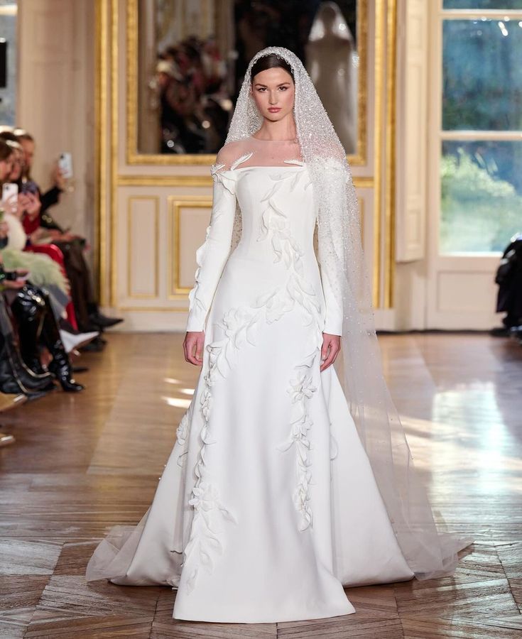 a woman in a white wedding dress with a veil on her head is walking down the runway