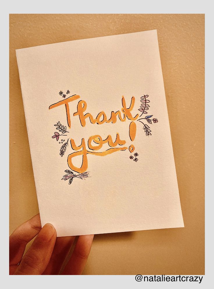 a hand holding up a thank card with the words thank you written on it in orange ink