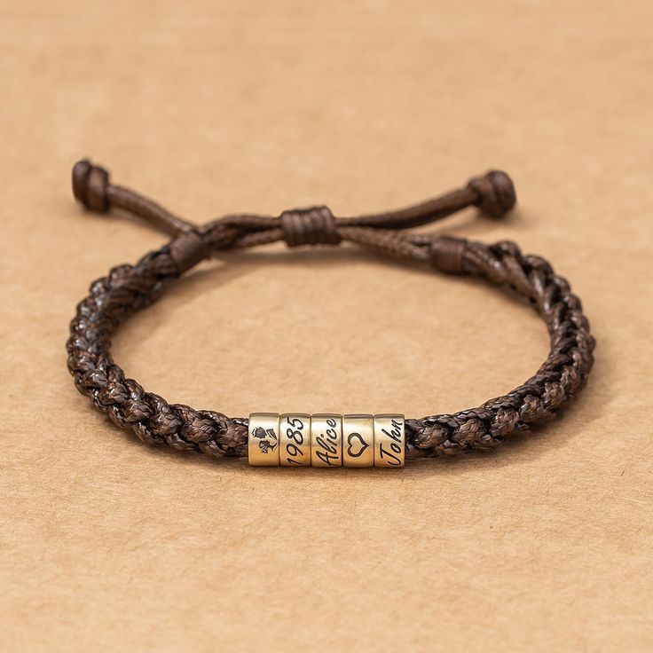 a brown leather bracelet with two gold bars on the clasp and an inscription that says love