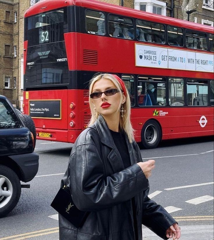 a woman in black jacket and sunglasses standing next to a red double decker bus