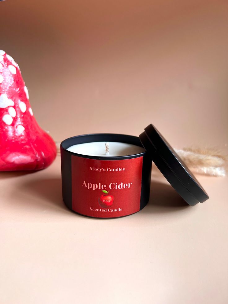 an apple cider candle sits next to a red heart shaped object on a table