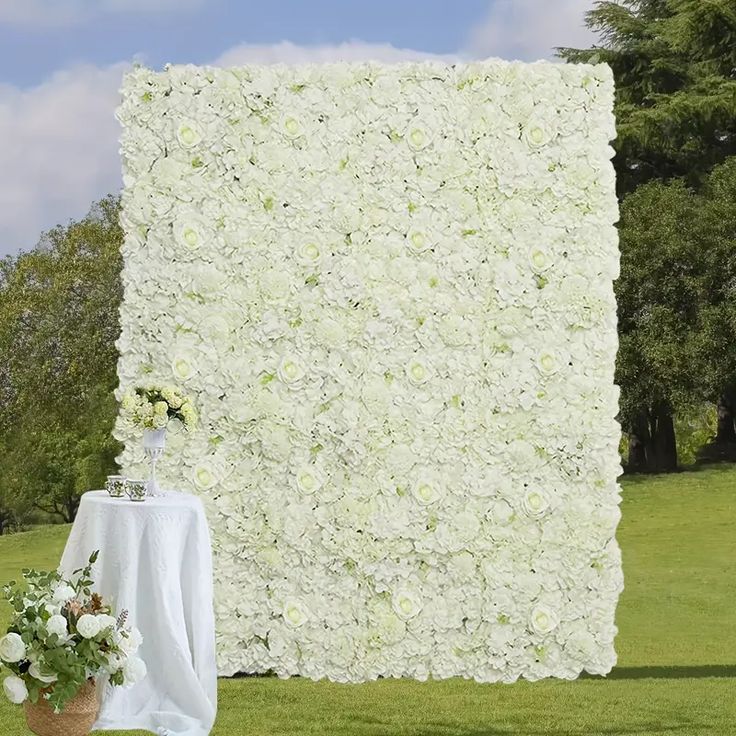 a large white flower covered wall next to a table with flowers on it and a vase