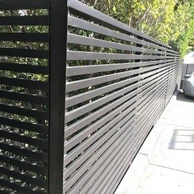 a black metal fence on the side of a sidewalk next to a white car and trees