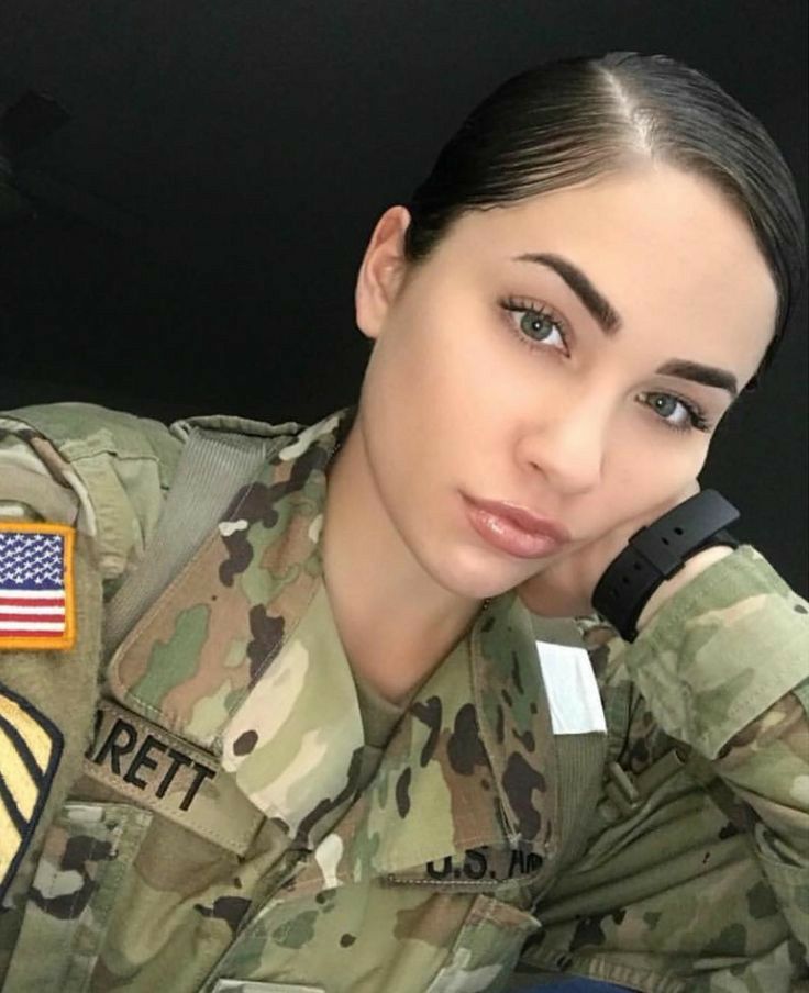 a woman in uniform is talking on her cell phone while sitting next to an american flag