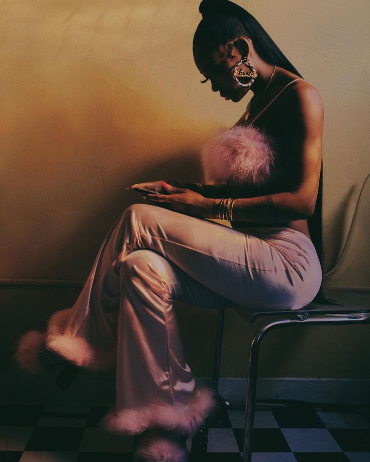 a woman is sitting on a chair and looking at her cell phone while wearing fur