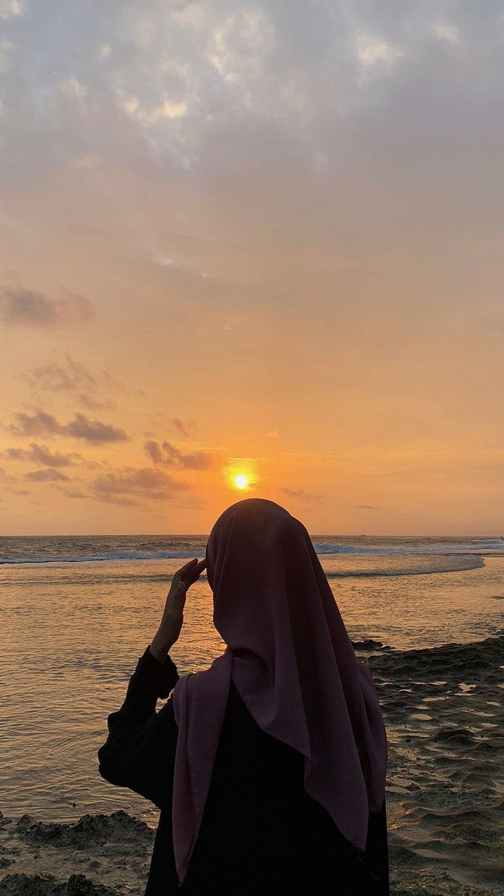 a woman standing on top of a sandy beach next to the ocean at sun set