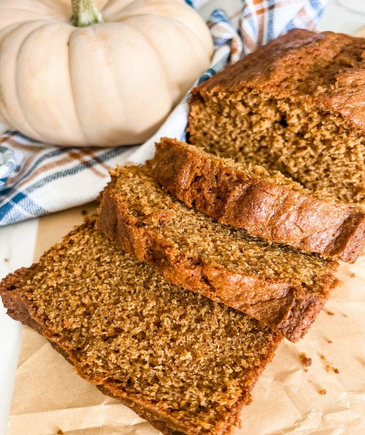 three slices of banana bread sitting on top of parchment paper next to a white pumpkin