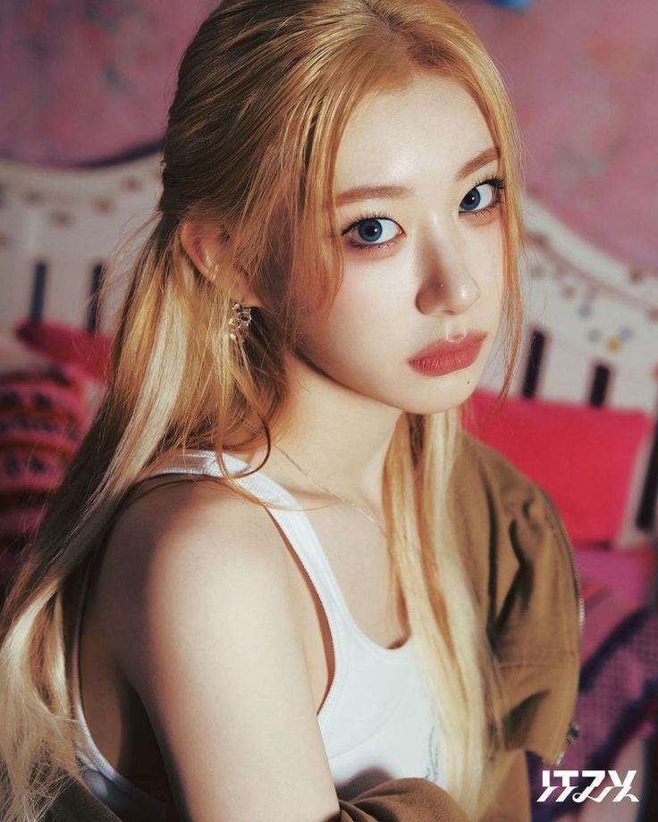 a woman with long blonde hair and blue eyes sitting on a pink couch wearing a white tank top