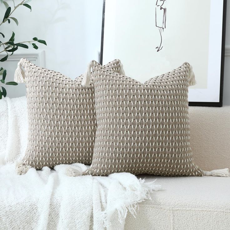 two pillows sitting on top of a white couch next to a plant in a vase