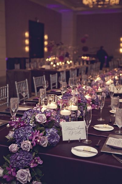 the tables are set up with purple flowers and candles for an elegant wedding reception or special event