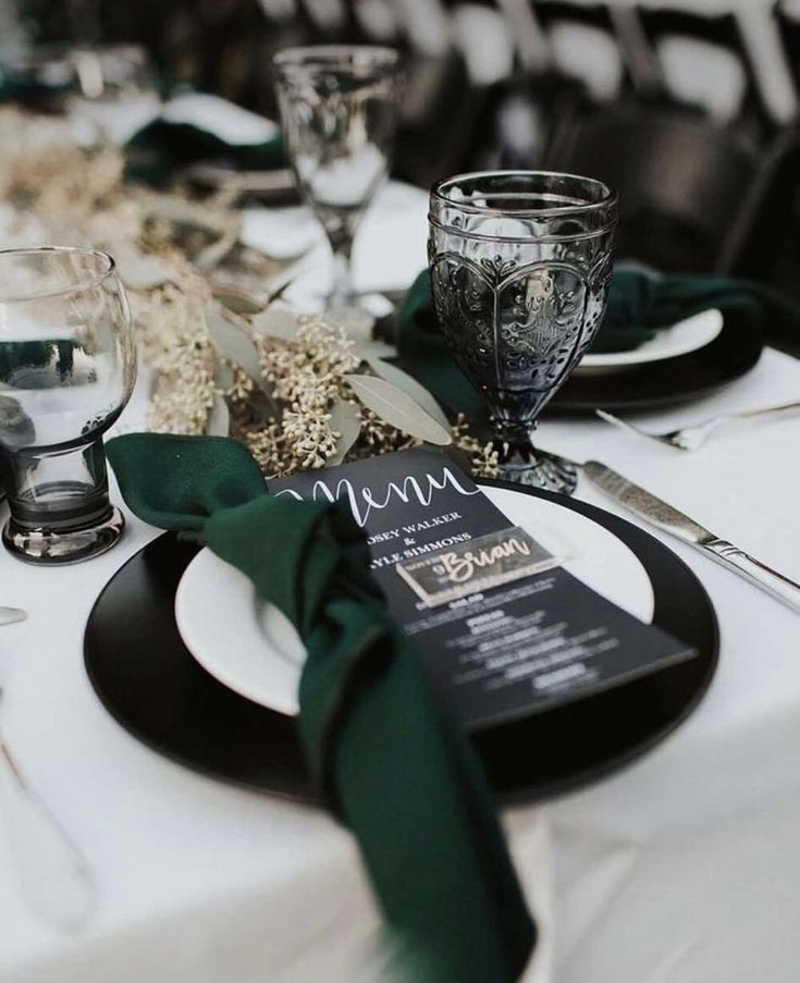 the table is set with black and white plates, silverware, and green napkins