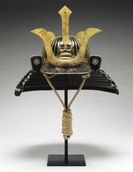 an elaborate helmet with gold decoration on the front and side, sitting on a black stand