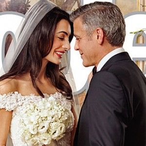 a man and woman standing next to each other in front of a wall with flowers