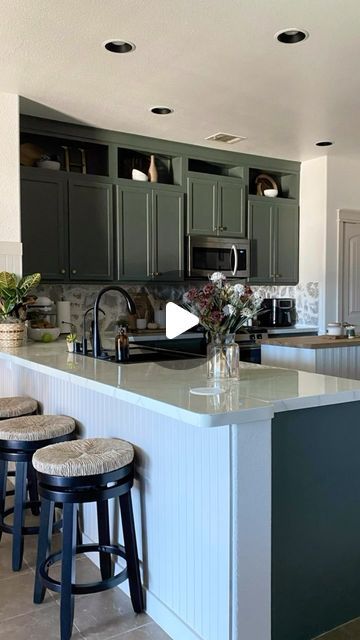 a kitchen with two stools and an island in the middle of it, surrounded by green cabinets