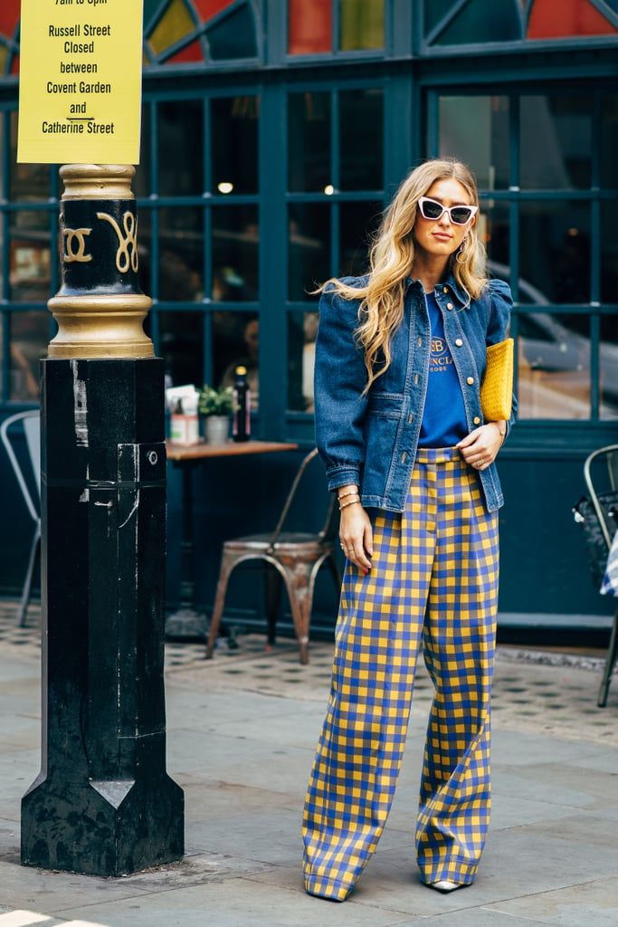 a woman standing next to a lamp post on the sidewalk wearing plaid pants and a denim jacket