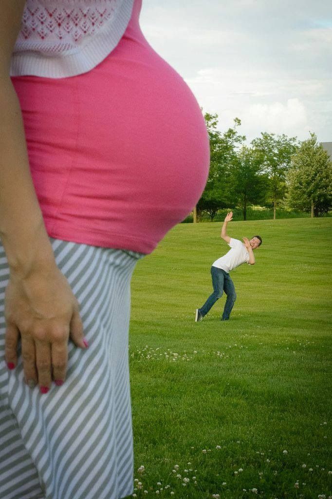 a pregnant woman standing on top of a lush green field