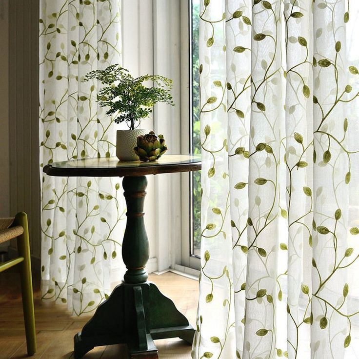 a small table with a potted plant on it in front of a curtained window