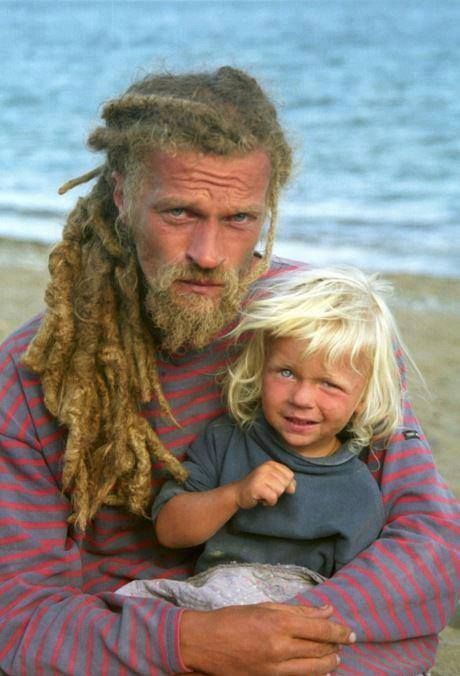 a man with dreadlocks holding a child on the beach