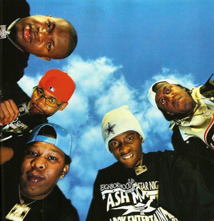 four men standing in front of a blue sky with clouds behind them and one man wearing a red beanie