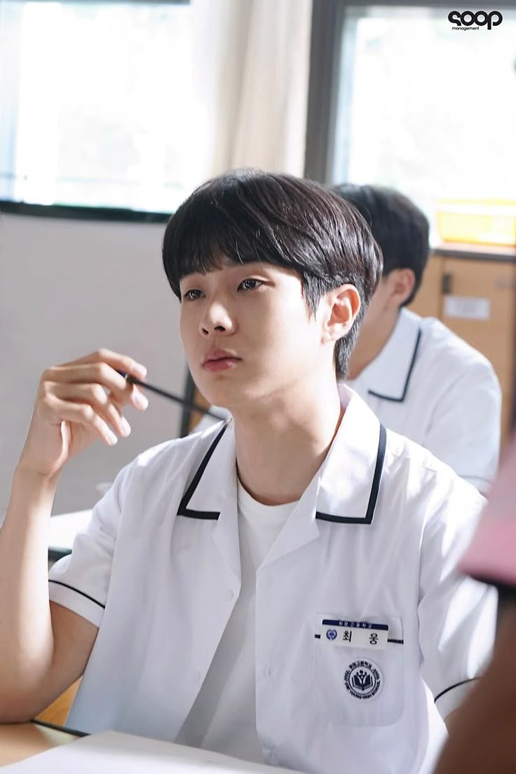 a young man sitting at a table in front of another person with his hand on his chin