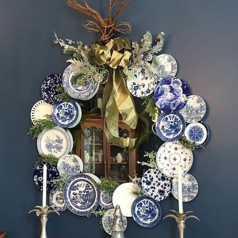 a blue and white christmas wreath on the wall with plates, candles and decorations around it